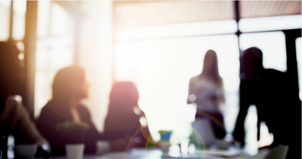 Faded image of people in a board room sitting and standing whilst in discussion