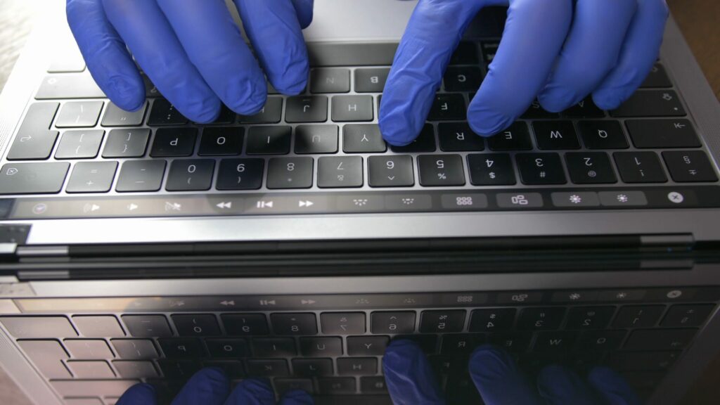 Doctor's Hands In Blue Surgical Gloves Typing On Laptop Keyboard